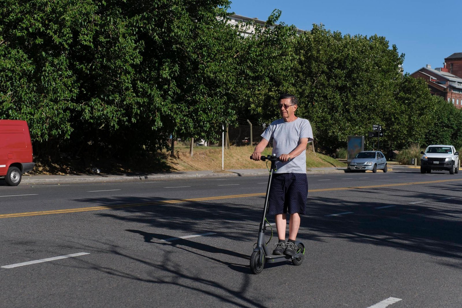 Man riding electric scooter on city street with cars and trees in background