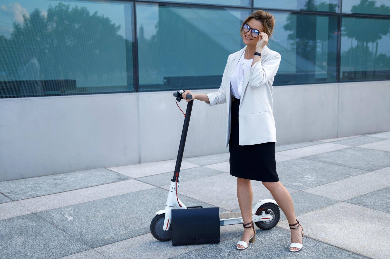 Businesswoman in a white blazer standing with an electric scooter and a briefcase, representing eco-friendly urban commuting.