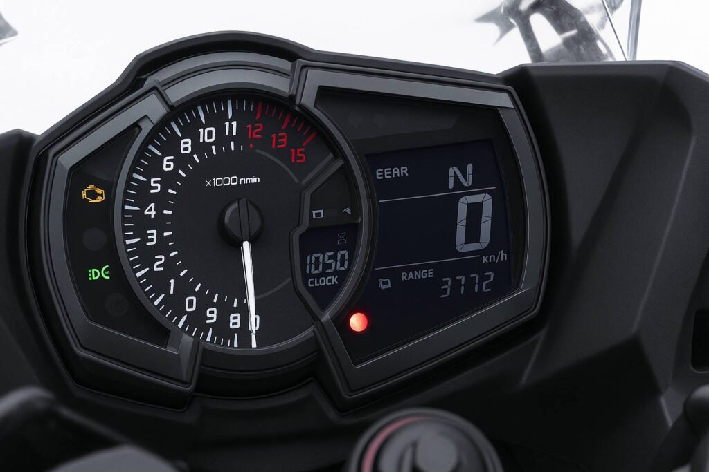Close-up view of a motorcycle digital instrument cluster displaying tachometer, clock, gear position, speedometer, range, and various warning indicators.
