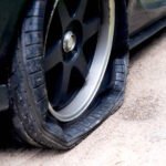 Close-up of a flat car tire on a dirt roadside, showing damaged rubber and deflated tread