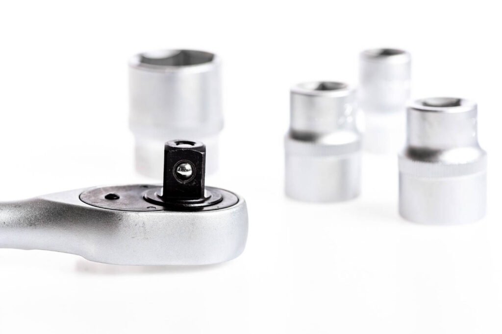 Close-up view of a ratchet wrench head and several metallic socket attachments placed on a clean white surface, ideal for mechanical or motorcycle maintenance tasks. 