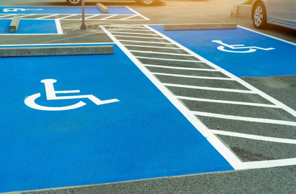 Bright blue accessible parking spaces marked with white wheelchair symbols and adjacent diagonal striped access aisles in a parking lot. The image shows the designated spaces with proper markings that provide extra room for wheelchair users to safely enter and exit vehicles.