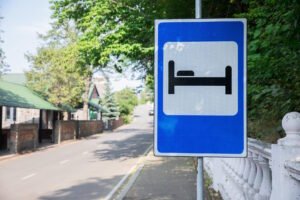 Blue service sign with white hospital bed symbol indicating nearby medical facilities on a tree-lined road