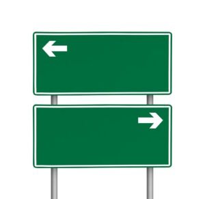 Two green rectangular road signs on poles; the top sign features a left-pointing white arrow, and the bottom sign features a right-pointing white arrow, both indicating directional guidance for drivers.