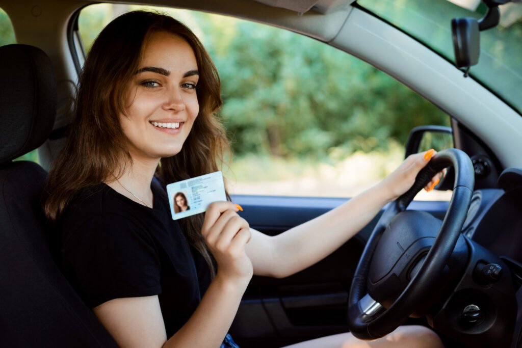 A person sitting in a car holding a driver's license ID card while smiling at the camera, representing modern driver licensing in America.