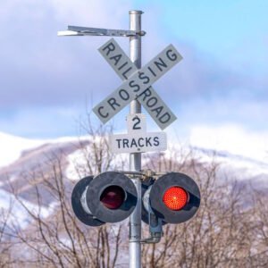 A railroad crossing sign with a crossbuck labeled "RAILROAD CROSSING" and an additional sign indicating "2 TRACKS," accompanied by flashing red warning lights, alerting drivers and pedestrians to stop for an approaching train.