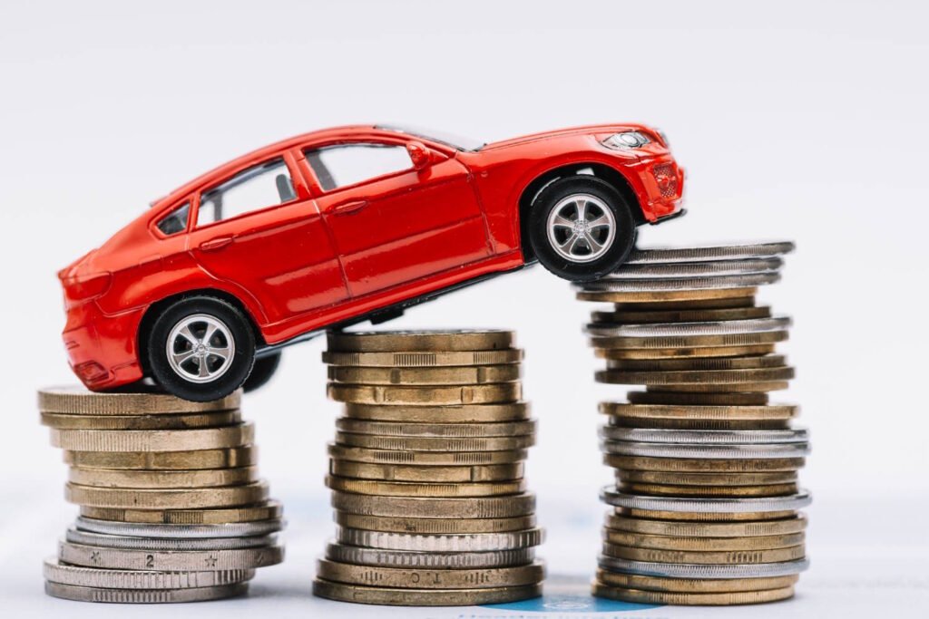 A small red toy car positioned on an ascending path of three stacks of coins, symbolizing increasing automobile expenses or car financing.