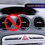 Car dashboard showing air conditioning vents with a red prohibition symbol over the center vent, indicating AC malfunction. Text overlay reads "AC NOT WORKING IN CAR" in yellow letters on a blue background.