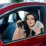 Smiling woman in red car holding car keys and cash, representing financial freedom after using traceloans.com student loans platform.
