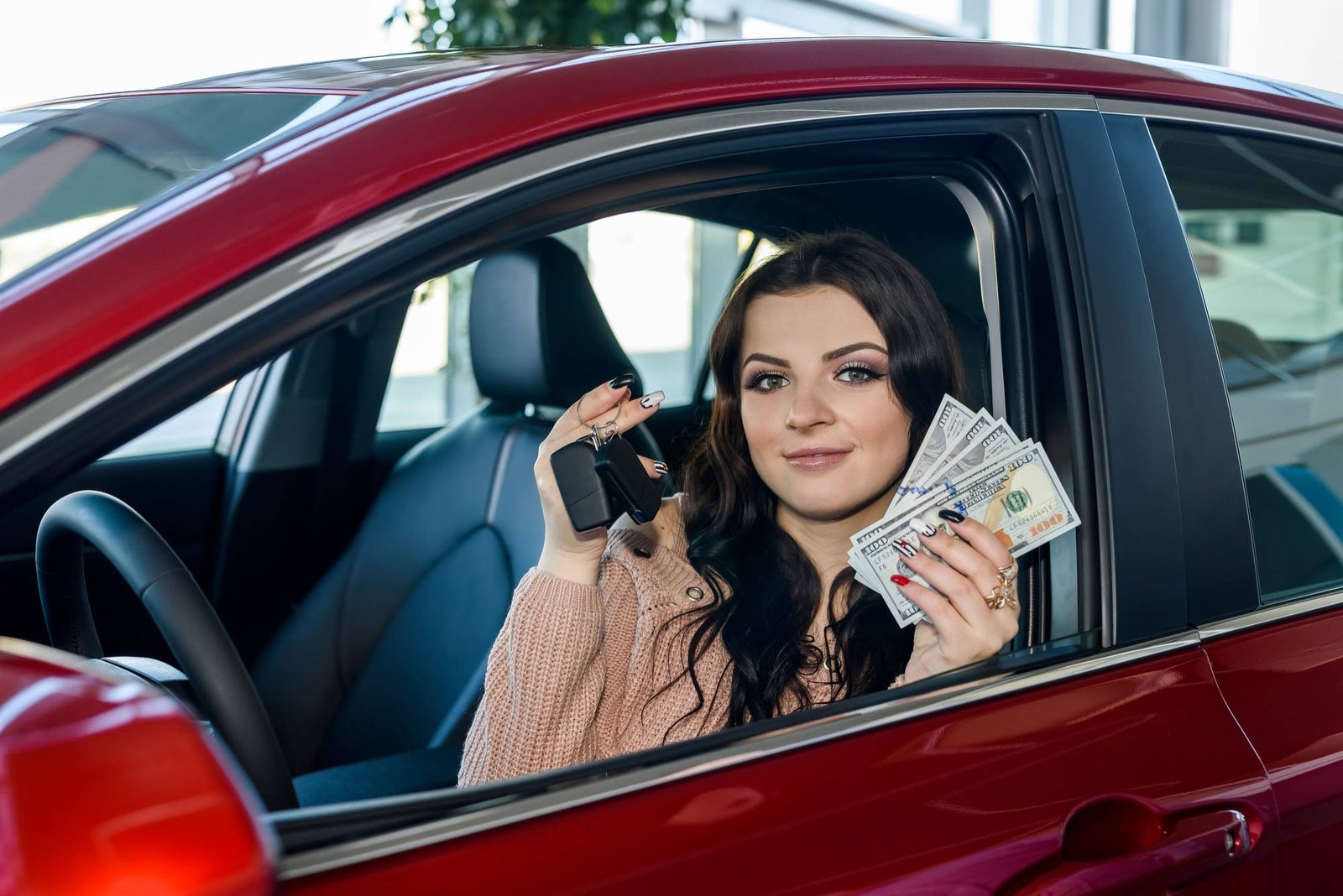 Smiling woman in red car holding car keys and cash, representing financial freedom after using traceloans.com student loans platform.