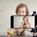 Content creator using smartphone to film videos demonstrating AI influencer generators technology with social media engagement icons