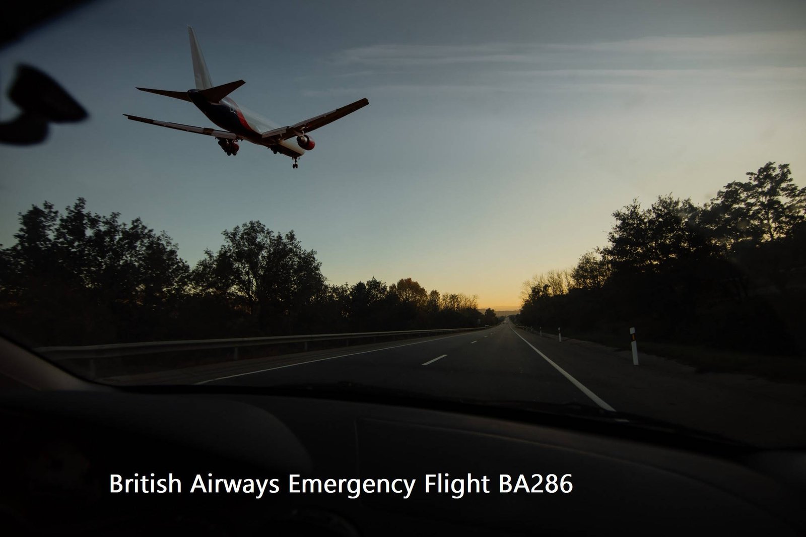 Commercial aircraft flying low over highway during emergency approach at dusk with trees silhouetted against twilight sky