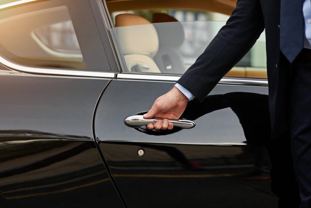Professional chauffeur in dark suit opening luxury car door showing premium chauffeur service experience