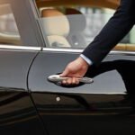 Professional chauffeur in dark suit opening luxury car door showing premium chauffeur service experience
