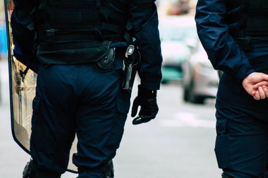 Two police officers in dark uniforms standing beside a police vehicle, showing professional law enforcement equipment and gear