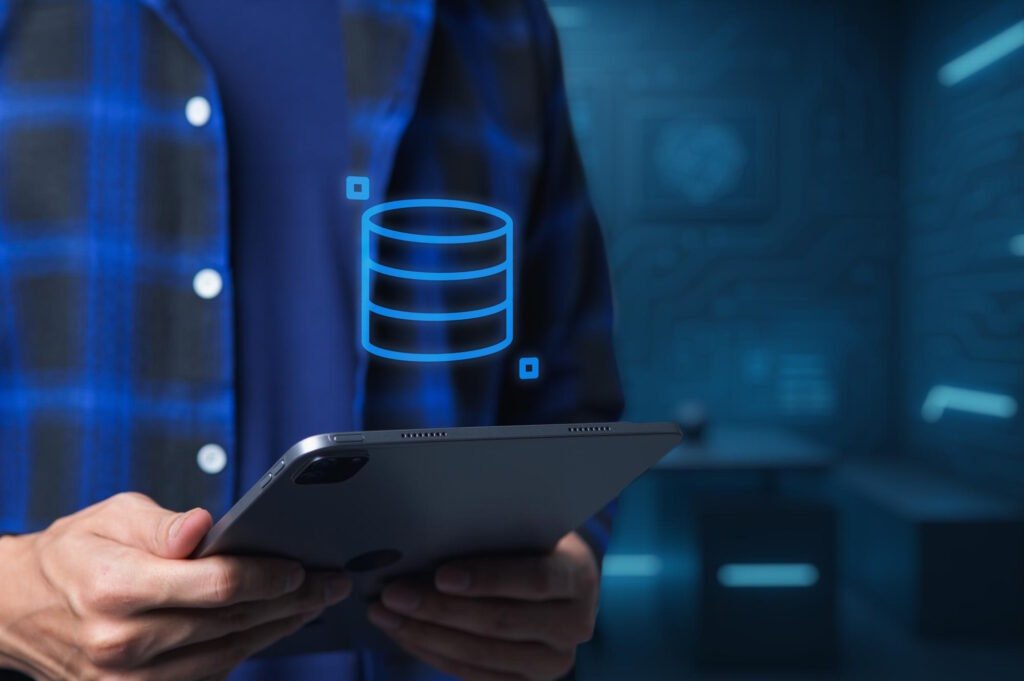 Hand holding tablet displaying blue database icon with glowing data visualization elements in modern tech environment