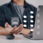 Professional demonstrating cloud storage management with digital folders and files flowing from laptop to cloud infrastructure.