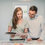 Young couple planning home renovation looking at color palette samples and design materials on kitchen counter in bright modern home