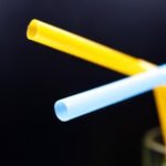 Close-up of bent yellow and light blue thermoplastic tubes or rods against a dark background, demonstrating the flexibility and moldability of thermoplastic materials.