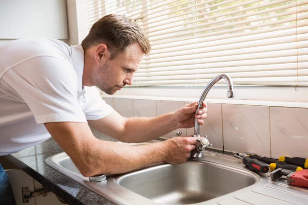 Man in white shirt repairing tap with tools on counter, demonstrating DIY faucet repair process.