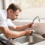 Man in white shirt repairing tap with tools on counter, demonstrating DIY faucet repair process.