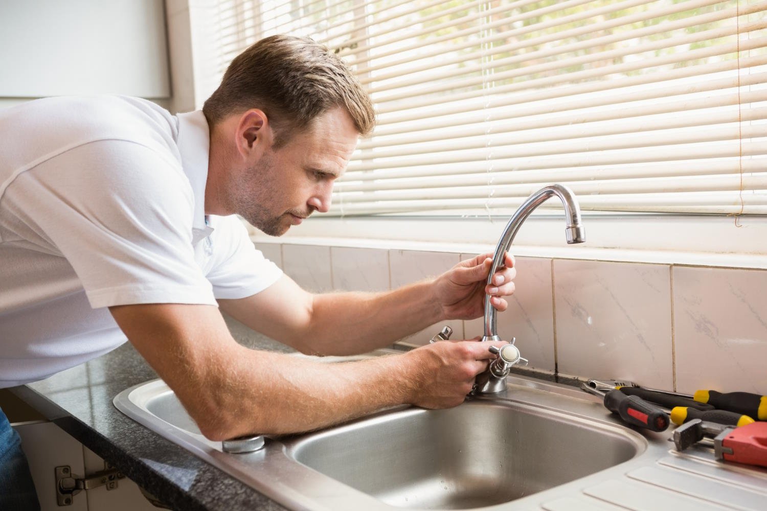 Man in white shirt repairing tap with tools on counter, demonstrating DIY faucet repair process.