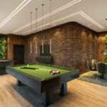 Modern luxury game room featuring a sleek black pool table with green felt, exposed brick accent wall, LED strip ceiling lighting, living plant walls, wooden paneling, and contemporary dining area with gray chairs