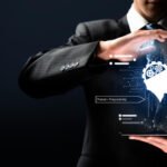 A businessman in a suit holds a digital hologram of an AI assistant icon above a tablet, symbolizing artificial intelligence, innovation, and business technology integration.