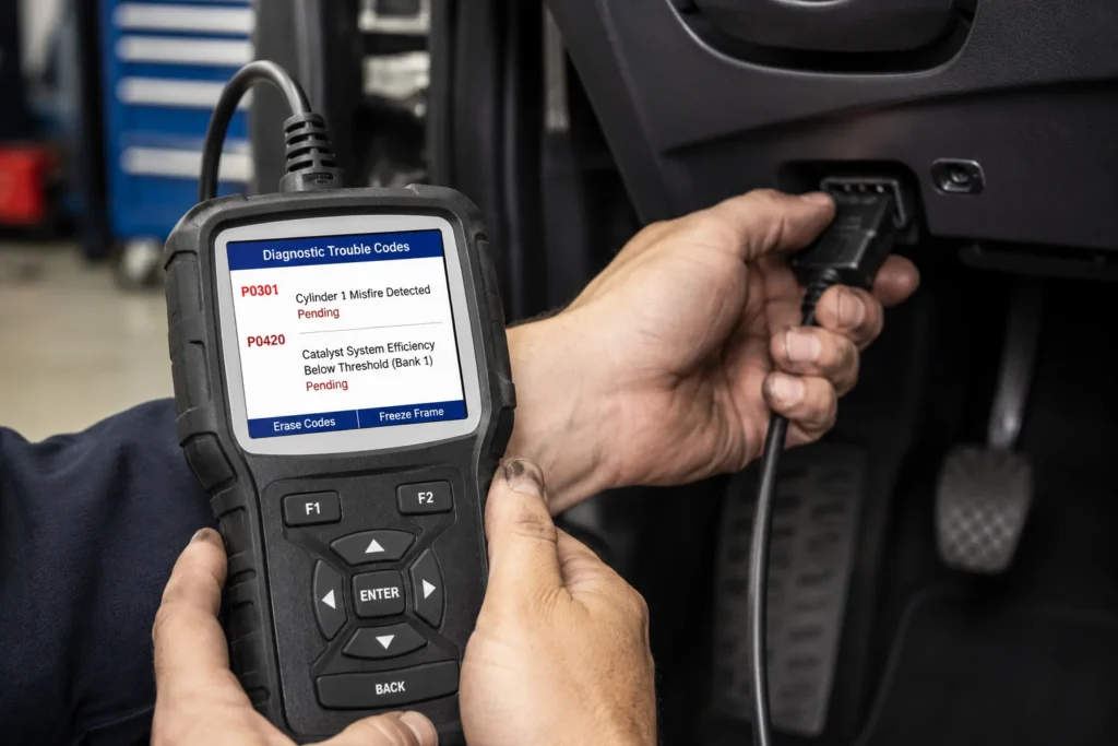Mechanic plugging OBD-II scanner into car diagnostic port showing P0301 and P0420 trouble codes on screen